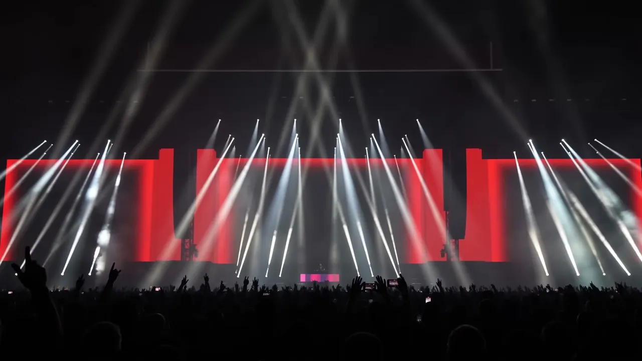 A wall of white beams over a red LED stage and a packed festival crowd.